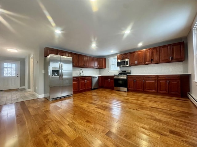 kitchen with light wood-type flooring, appliances with stainless steel finishes, backsplash, and sink