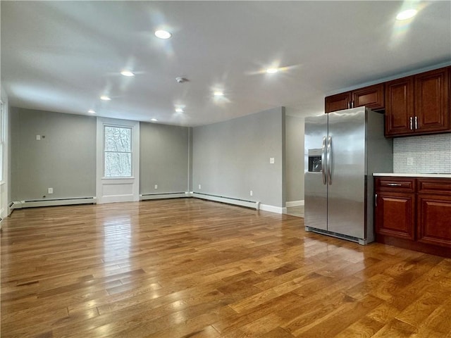 kitchen featuring baseboard heating, wood-type flooring, stainless steel fridge, and tasteful backsplash