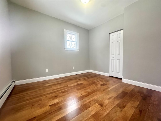 unfurnished room featuring baseboard heating and wood-type flooring