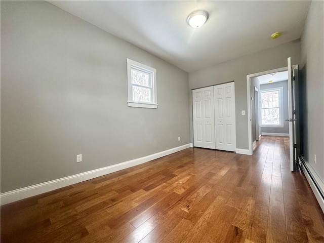 unfurnished bedroom featuring baseboard heating, a closet, and hardwood / wood-style floors