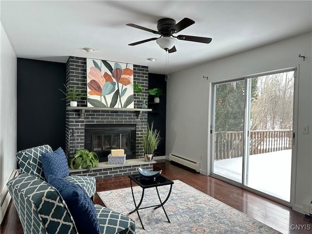 living room with a brick fireplace, a baseboard radiator, dark hardwood / wood-style flooring, and ceiling fan