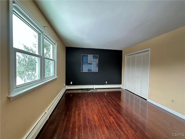 unfurnished bedroom featuring a baseboard heating unit, a closet, and hardwood / wood-style flooring