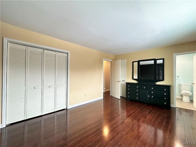 unfurnished bedroom with ensuite bathroom, a closet, and dark hardwood / wood-style flooring