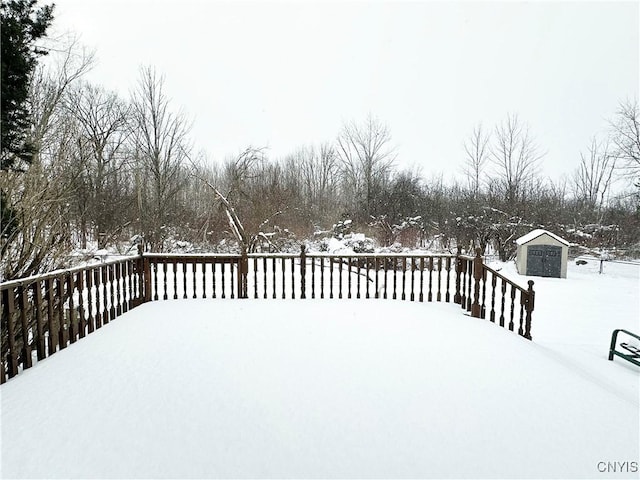 snowy yard with a storage shed and a deck