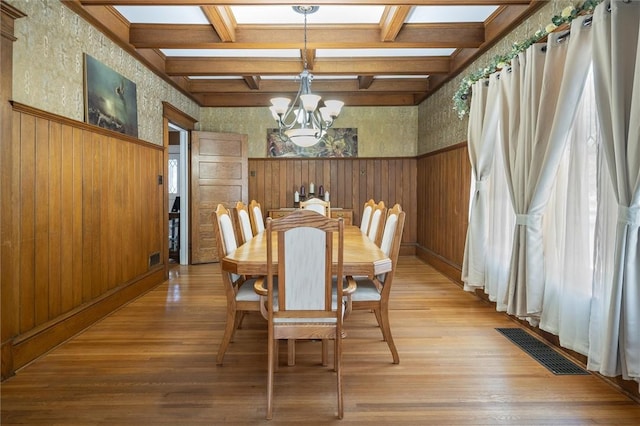 dining area with wood-type flooring, a notable chandelier, beamed ceiling, and coffered ceiling