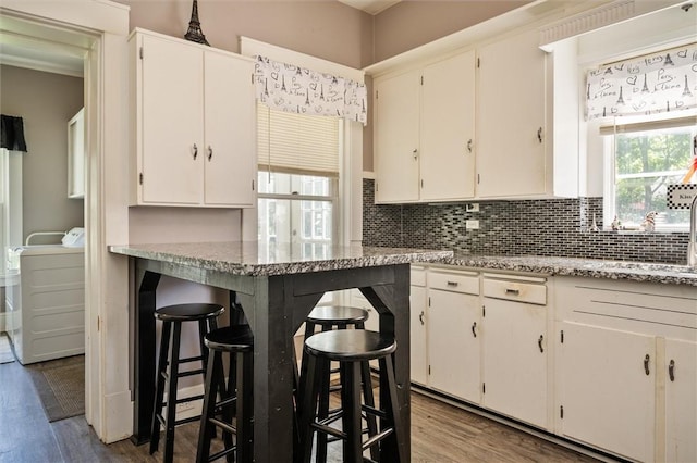 kitchen featuring hardwood / wood-style floors, white cabinets, tasteful backsplash, a kitchen breakfast bar, and light stone counters