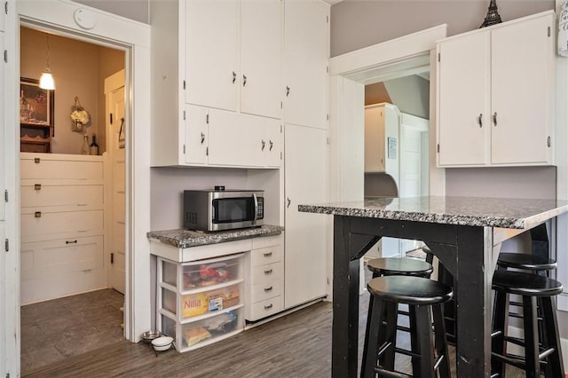 kitchen with a breakfast bar area, dark hardwood / wood-style flooring, white cabinets, and light stone countertops