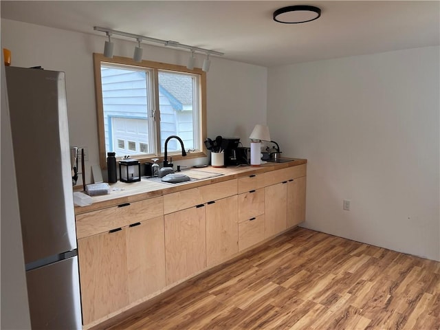 kitchen with light wood-type flooring, sink, light brown cabinetry, and stainless steel refrigerator