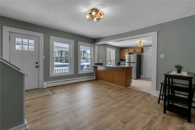 kitchen featuring light hardwood / wood-style floors, a baseboard radiator, stainless steel fridge, and kitchen peninsula