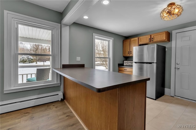 kitchen featuring beamed ceiling, kitchen peninsula, a baseboard radiator, and stainless steel refrigerator