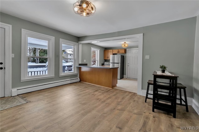 kitchen with light wood-type flooring, kitchen peninsula, stainless steel fridge, and a baseboard radiator