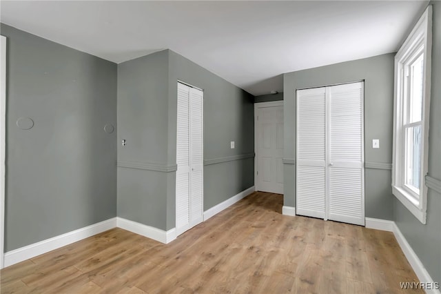 unfurnished bedroom with light wood-type flooring and multiple closets