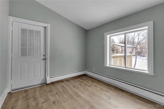 spare room with vaulted ceiling, baseboard heating, and light hardwood / wood-style flooring