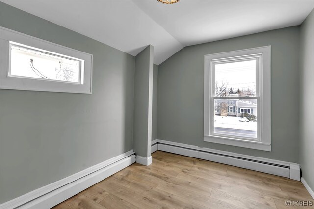 empty room featuring lofted ceiling, light hardwood / wood-style flooring, and a baseboard radiator