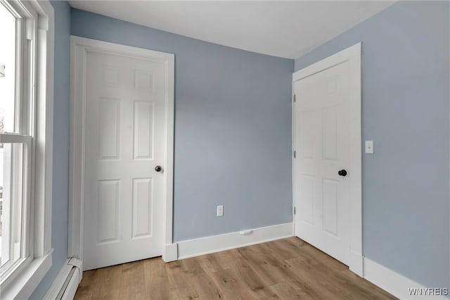 unfurnished bedroom with a closet, multiple windows, light hardwood / wood-style flooring, and a baseboard radiator