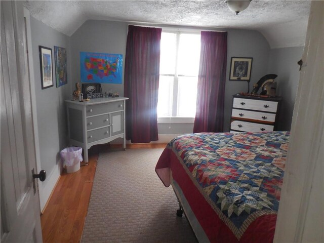 bedroom with hardwood / wood-style flooring, multiple windows, a textured ceiling, and vaulted ceiling