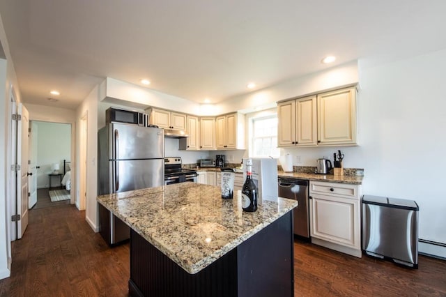 kitchen with cream cabinetry, stainless steel appliances, dark hardwood / wood-style flooring, light stone countertops, and a center island