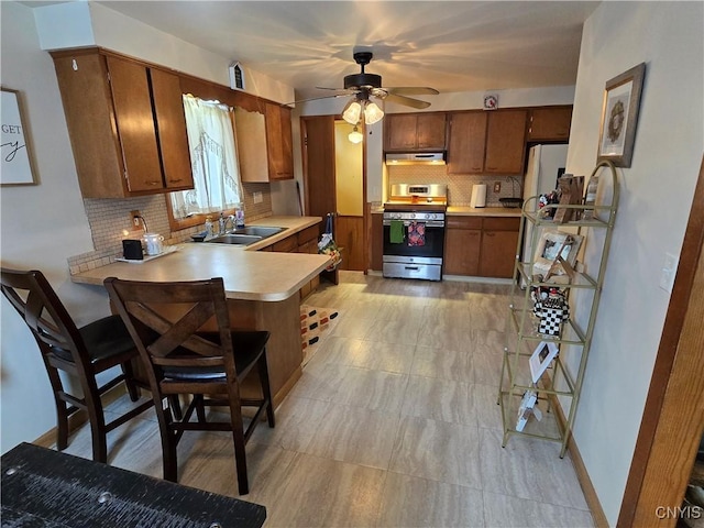 kitchen featuring refrigerator, a breakfast bar, kitchen peninsula, sink, and gas range