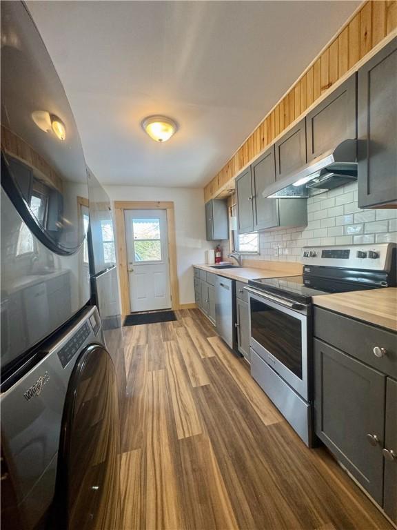 kitchen featuring stacked washing maching and dryer, appliances with stainless steel finishes, sink, and gray cabinetry