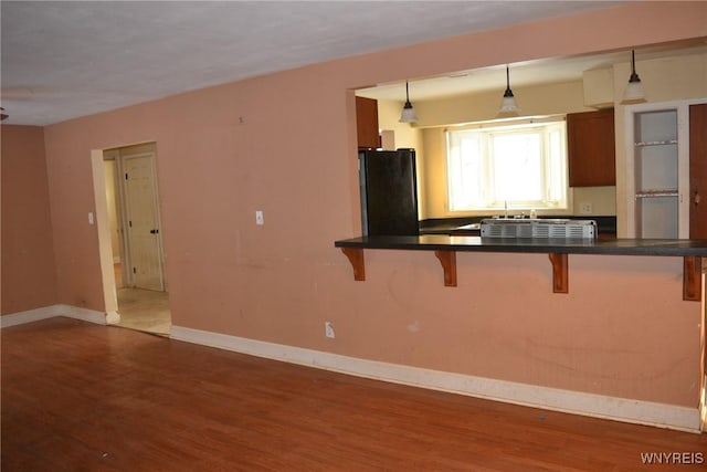 kitchen featuring dark hardwood / wood-style floors, kitchen peninsula, hanging light fixtures, a kitchen breakfast bar, and black refrigerator