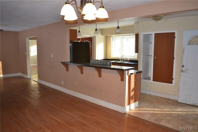 kitchen featuring pendant lighting, black fridge, kitchen peninsula, an inviting chandelier, and a kitchen breakfast bar