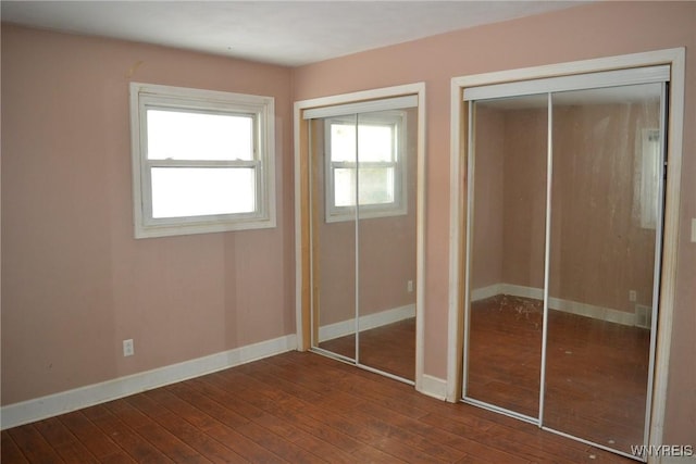 unfurnished bedroom with dark hardwood / wood-style flooring and two closets