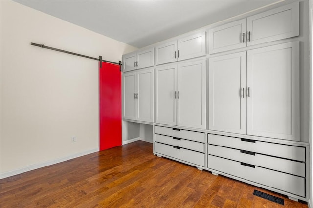 unfurnished bedroom featuring a barn door, a closet, and dark wood-type flooring