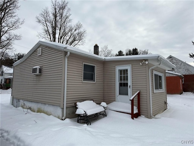 snow covered house featuring a wall mounted air conditioner