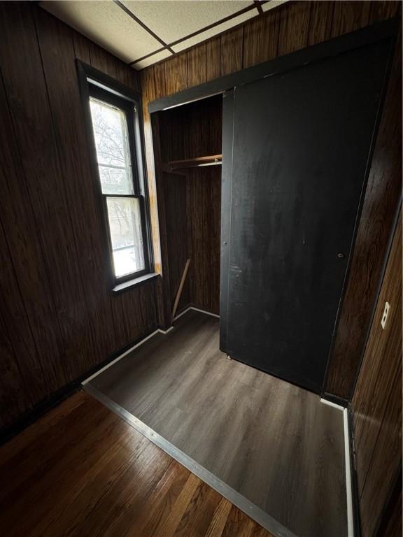 unfurnished bedroom with wooden walls, dark hardwood / wood-style flooring, and a closet