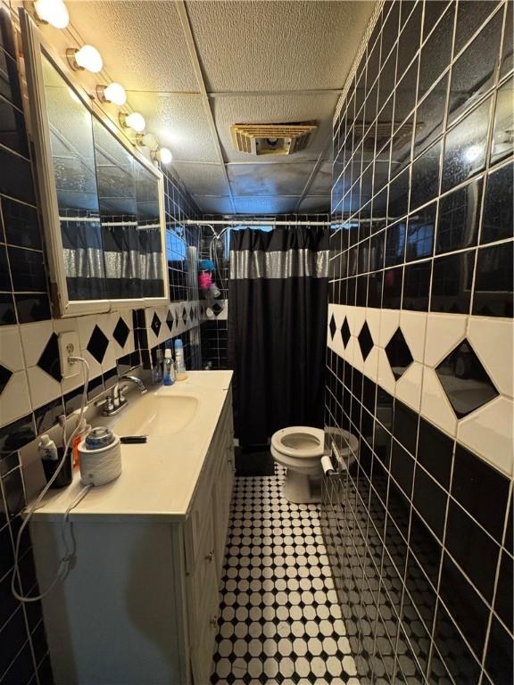 bathroom featuring walk in shower, vanity, toilet, and tile walls