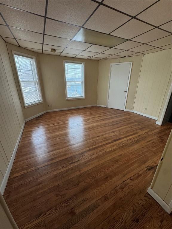 empty room featuring a healthy amount of sunlight, a paneled ceiling, and dark hardwood / wood-style flooring