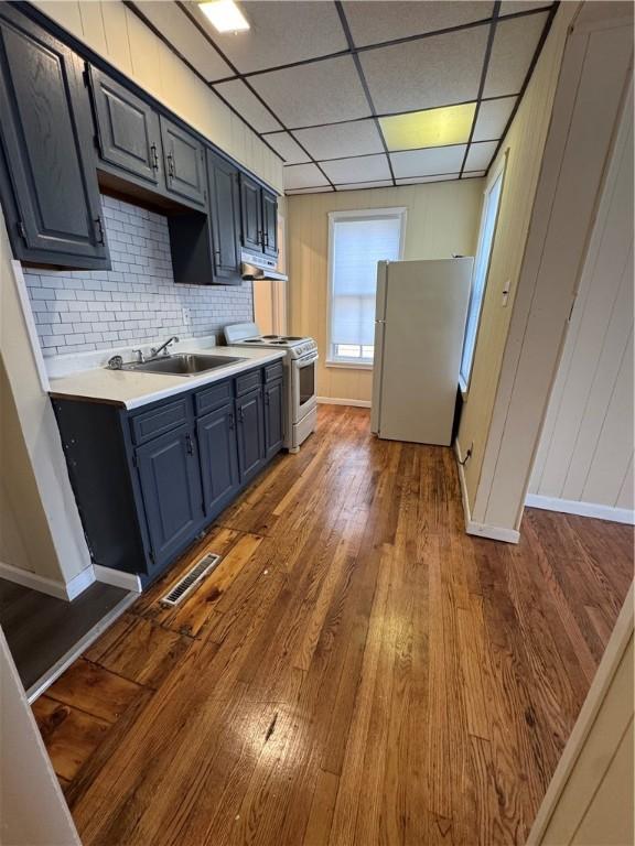 kitchen featuring a paneled ceiling, backsplash, hardwood / wood-style flooring, blue cabinetry, and white appliances