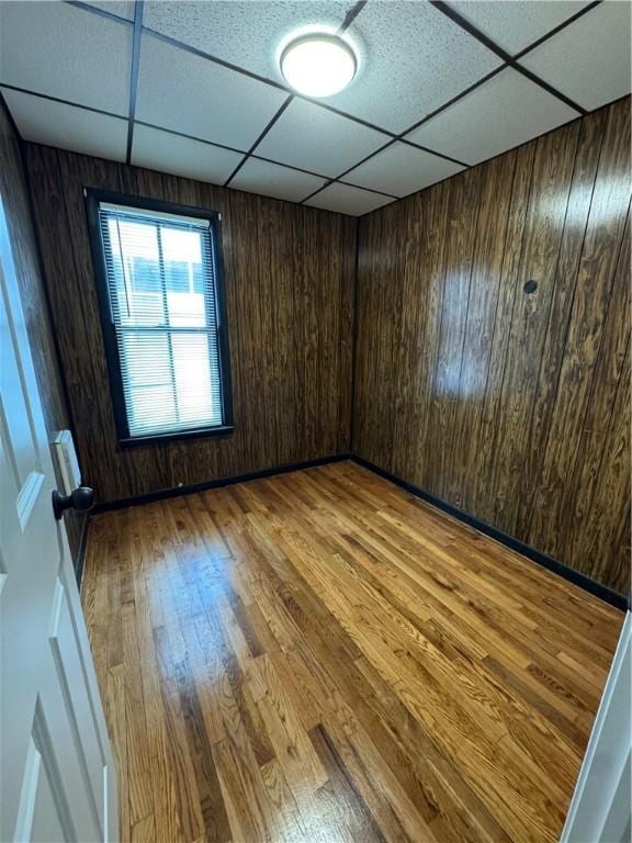 spare room with a paneled ceiling, hardwood / wood-style floors, and wood walls