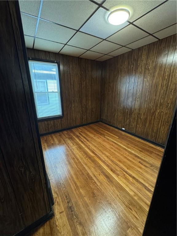 empty room featuring a paneled ceiling, wooden walls, and light wood-type flooring