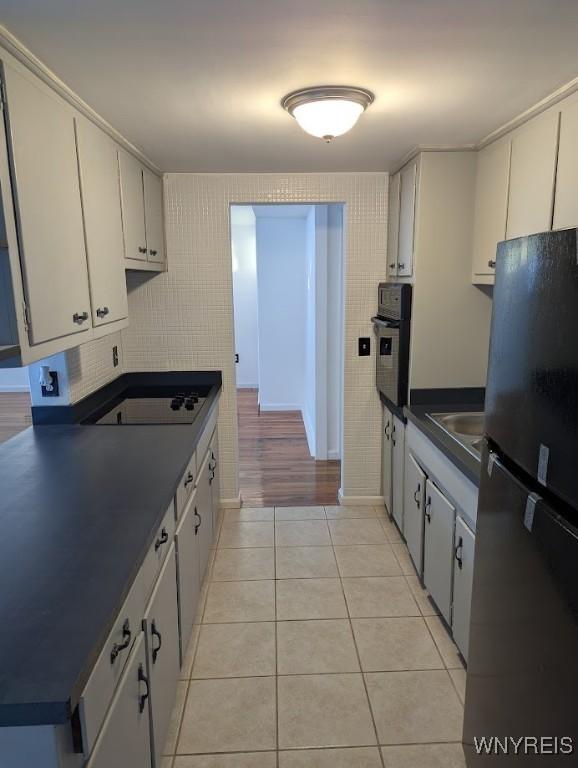 kitchen featuring sink, white cabinetry, light tile patterned floors, and black appliances