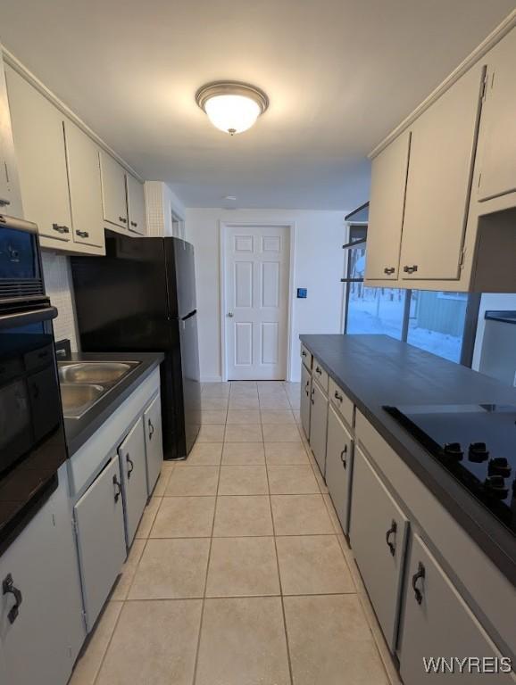 kitchen with light tile patterned floors, white cabinetry, sink, and black appliances