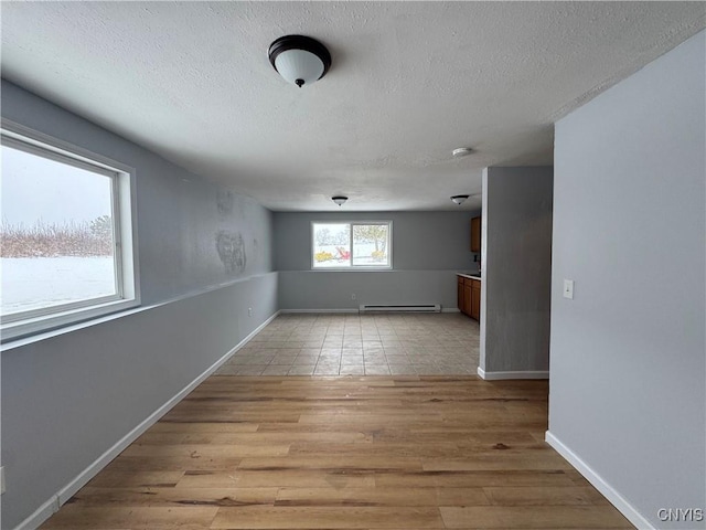 unfurnished room with light hardwood / wood-style floors, baseboard heating, and a textured ceiling