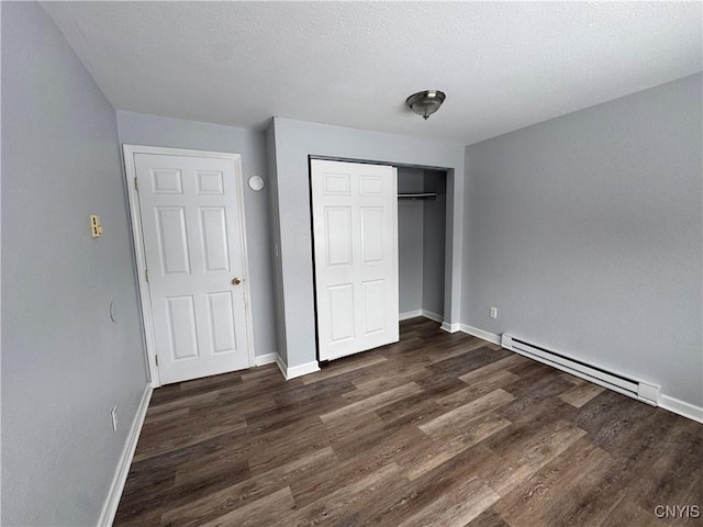 unfurnished bedroom with baseboard heating, a textured ceiling, dark hardwood / wood-style floors, and a closet