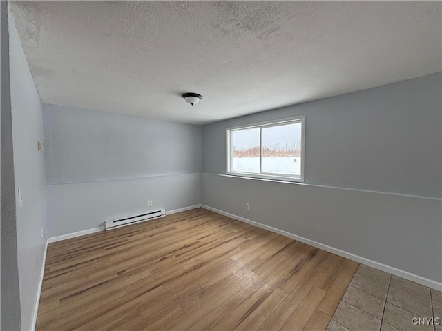 empty room with a textured ceiling, baseboard heating, and light hardwood / wood-style floors