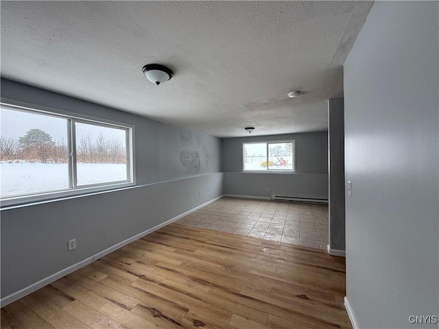 spare room with a baseboard heating unit, a textured ceiling, and light hardwood / wood-style flooring