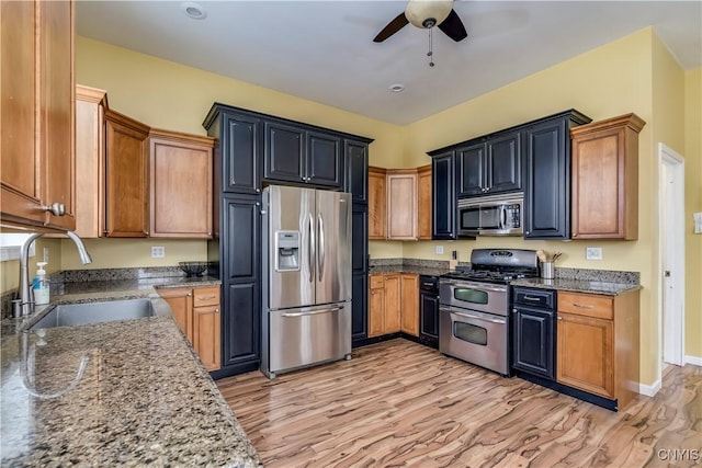 kitchen featuring ceiling fan, stainless steel appliances, dark stone countertops, and sink