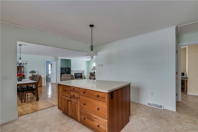 kitchen with decorative light fixtures, ceiling fan, a kitchen island, crown molding, and light stone counters