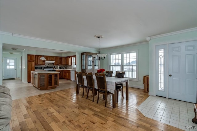 dining space with light hardwood / wood-style floors, ornamental molding, and an inviting chandelier