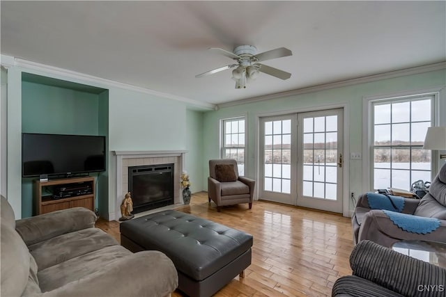 living room with ceiling fan, a tile fireplace, crown molding, and light hardwood / wood-style floors