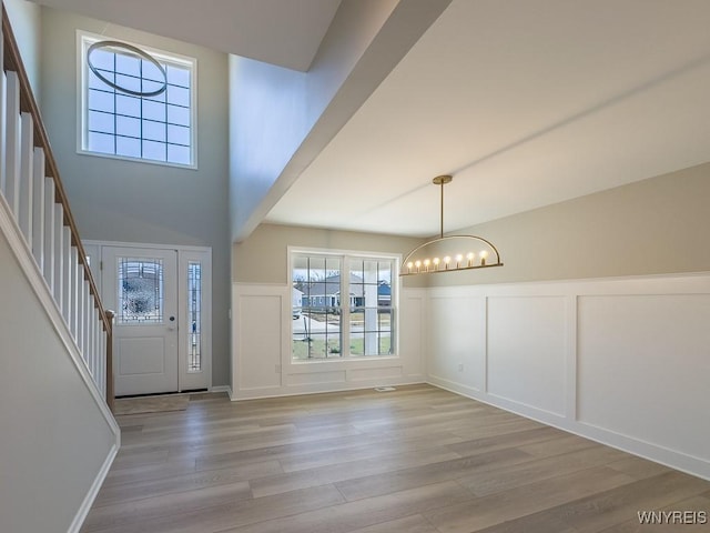 foyer with a chandelier, stairway, light wood-style flooring, wainscoting, and a decorative wall