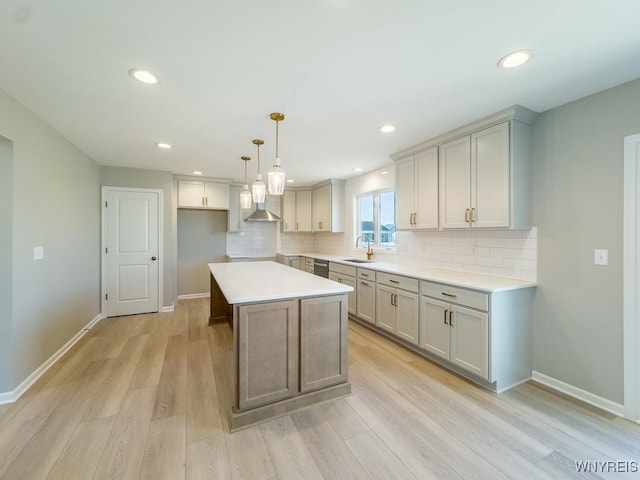 kitchen featuring backsplash, a kitchen island, wall chimney range hood, light wood-type flooring, and a sink