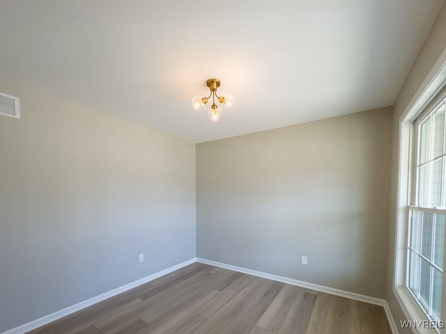 unfurnished room featuring an inviting chandelier, visible vents, wood finished floors, and baseboards