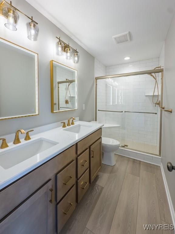 bathroom with visible vents, a stall shower, wood finished floors, and a sink