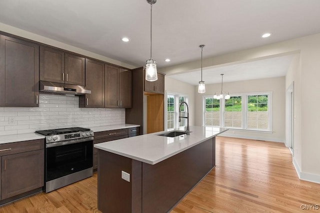 kitchen featuring decorative light fixtures, a center island with sink, decorative backsplash, sink, and stainless steel range with gas stovetop