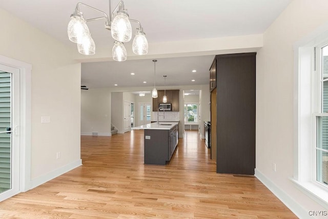 kitchen featuring dark brown cabinetry, decorative light fixtures, light hardwood / wood-style floors, decorative backsplash, and a center island with sink